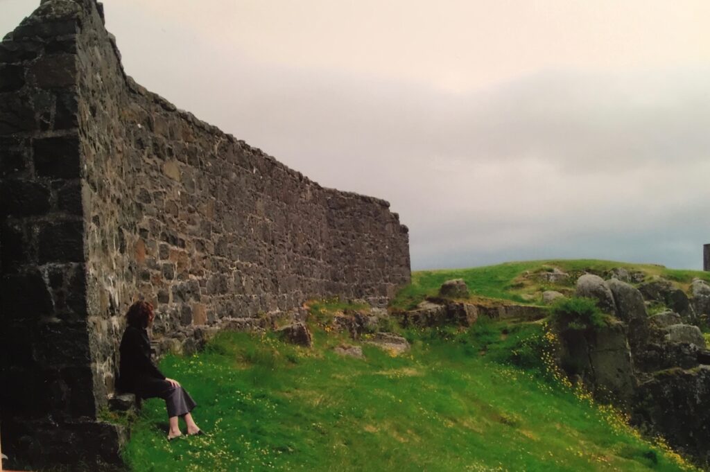 girl sitting by an old stone wall on a hilltop